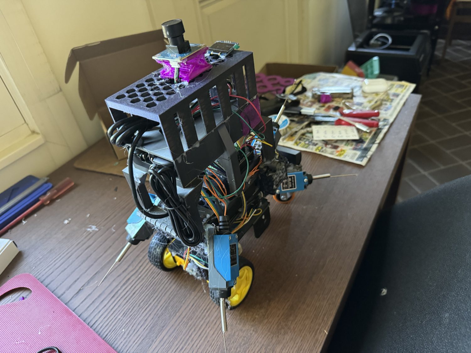 Side profile of the robot by a window, showing the stacked chassis, the single driven wheel, and a handwritten wiring note on the bench.